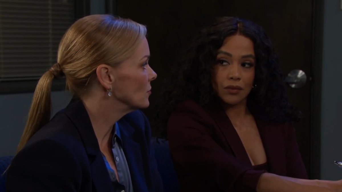 Two women, one blonde with a ponytail and another with dark curly hair, appear to be in conversation.
