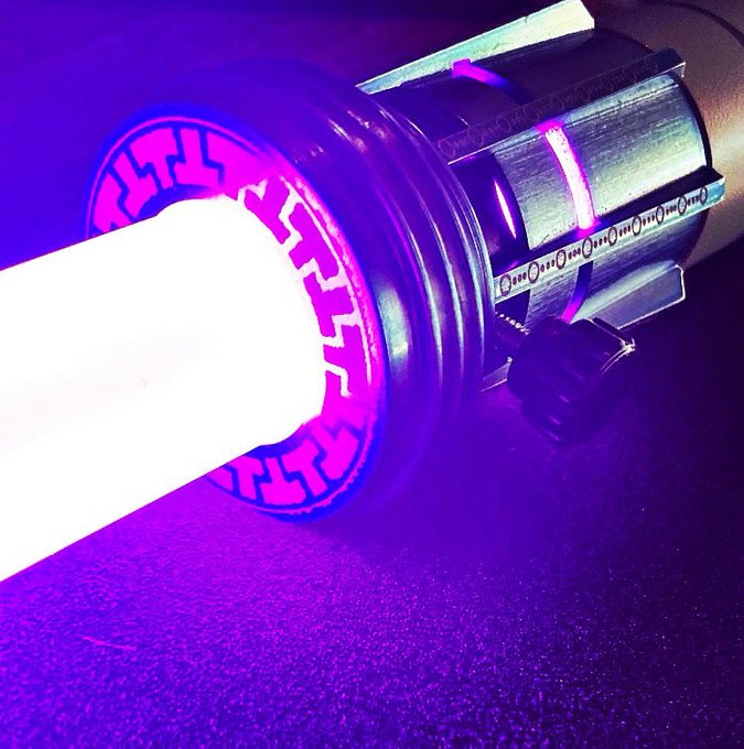 A close-up photo of a UV or LED light bulb illuminated with bright purple/violet light, showing the metallic base and the glowing diode element.