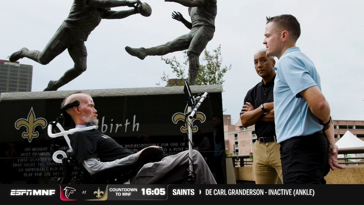 An emotional ESPN Monday Night Football scene with a man in a wheelchair receiving medical attention near a Saints statue, with the ticker reading 'COUNTDOWN TO MNF 16:05 SAINTS > DE CARL GRANDERSON - INACTIVE (ANKLE)'.