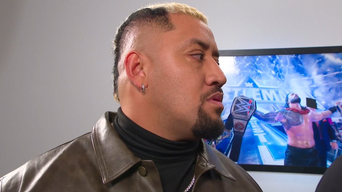 A man with a blonde-streaked mohawk and beard, wearing a leather jacket and black turtleneck, is shown in profile. Behind him, a TV screen displays a WrestleMania promotional image featuring a wrestler and championship belt, relating to the post about Solo not being searched in #WWERAW.