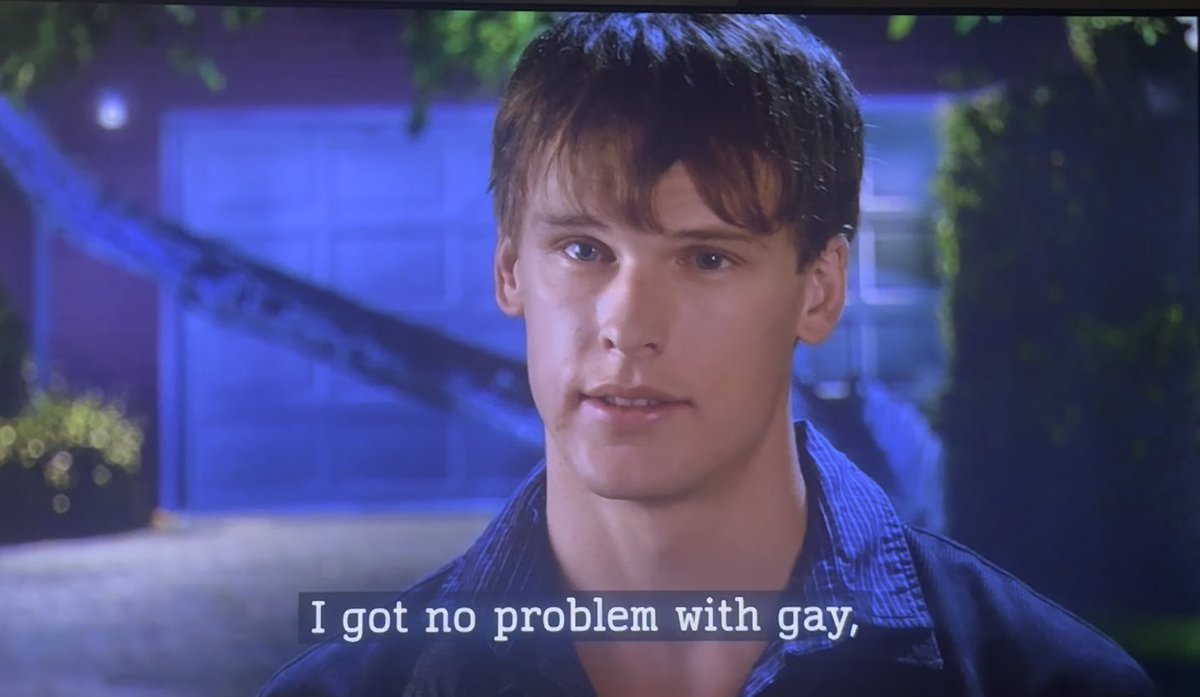 A close-up of a young man in a blue shirt being filmed outdoors at night, with the subtitle 'I got no problem with gay,' displayed at the bottom of the frame.