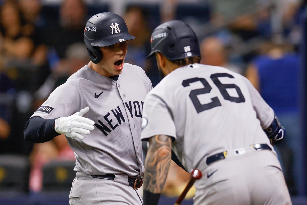 New York Yankees player #99 celebrates with teammate #26 in their road gray "NEW YORK" uniforms, with "STRAUSS" branding visible on their navy batting helmets. The image aligns with the caption referencing Ben Rice, capturing an animated moment of team celebration likely following a home run or key play.