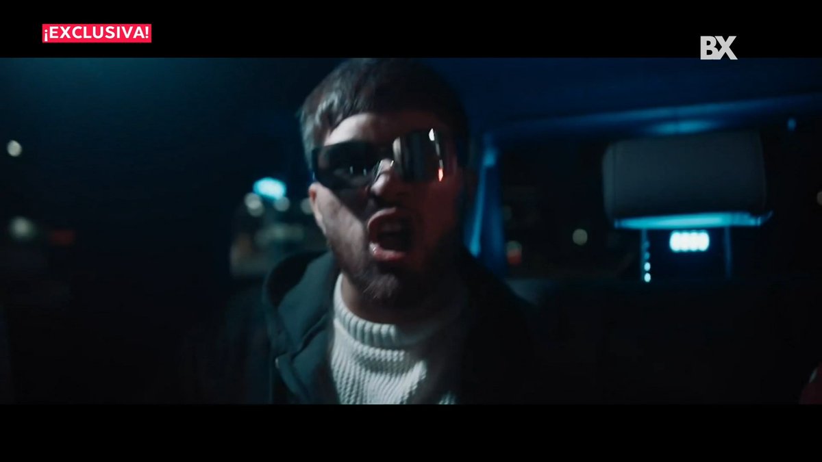 A bearded man wearing reflective sunglasses and a white sweater passionately sings or speaks inside what appears to be a vehicle at night. The image features "EXCLUSIVA!" text in the top left and "BX" logo in the top right, promoting content about Los Gemelos De Sinaloa and their new album "The Gemeliza" on the Qué News Bandamax program.