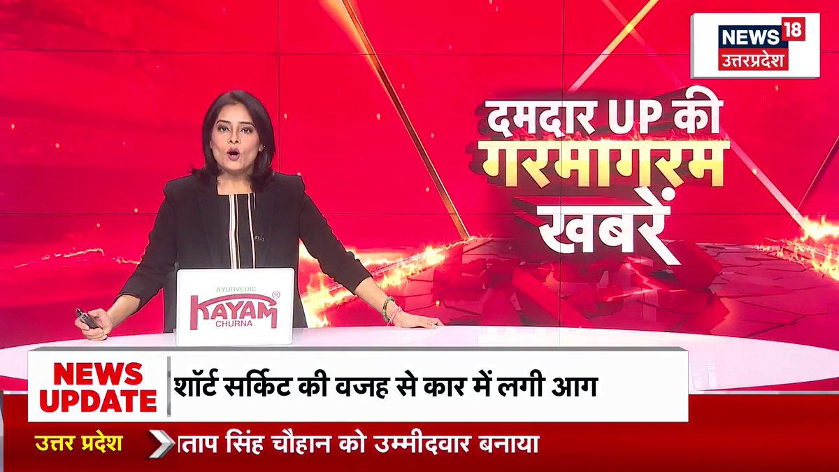 A news anchor delivers a broadcast on News18 Uttar Pradesh with Hindi text reading 'दमदार UP की गरमागरम खबरें' (Hot news of powerful UP) and a ticker stating 'शॉर्ट सर्किट की वजह से कार में लगी आग' (Car caught fire due to short circuit).