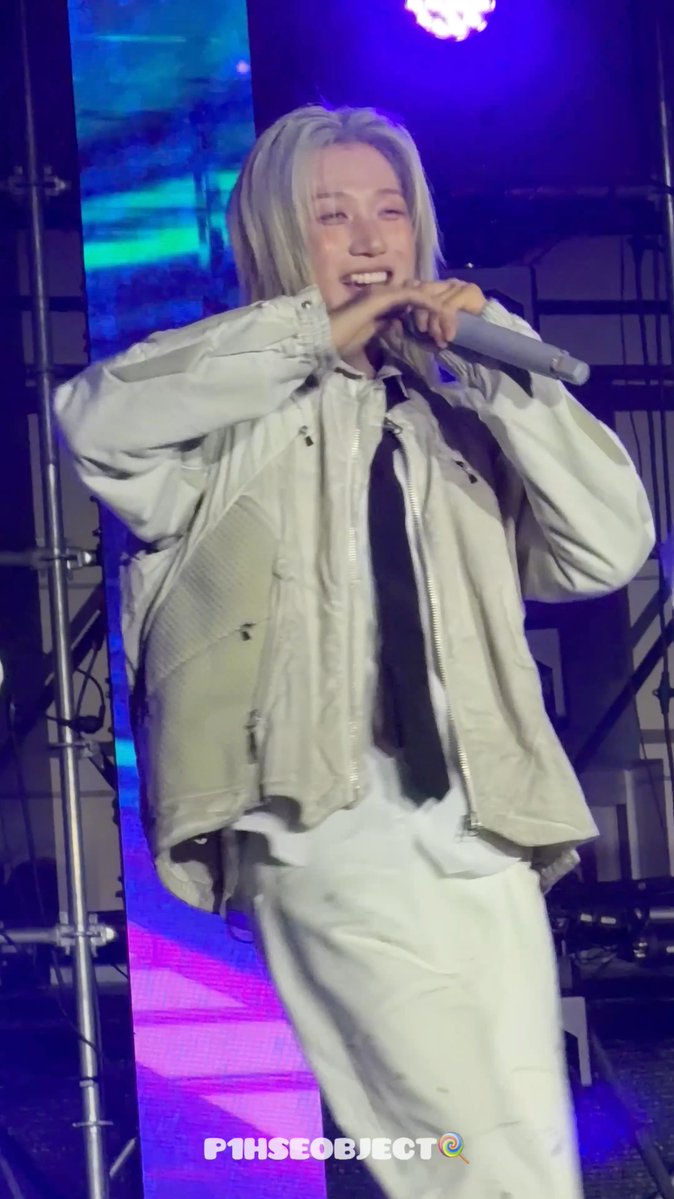 A performer with blonde hair in a white jacket holds a microphone on stage, with 'P1HSEOBJECT' watermark visible.