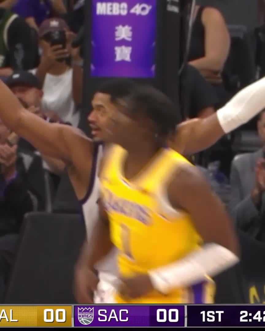 A screenshot from a basketball broadcast shows a Lakers player in a yellow jersey raising his arms in front of a Sacramento Kings bench; the score graphic at the bottom reads 'LAL 00 SAC 00 1ST 2:4' and a courtside advertisement displays 'MEBS 40'.