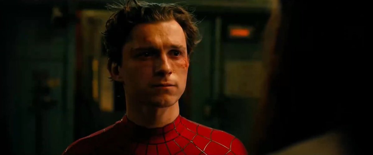 A scene from a Spider-Man movie showing a young man in the Spider-Man suit with a bruised face in a dimly lit room.