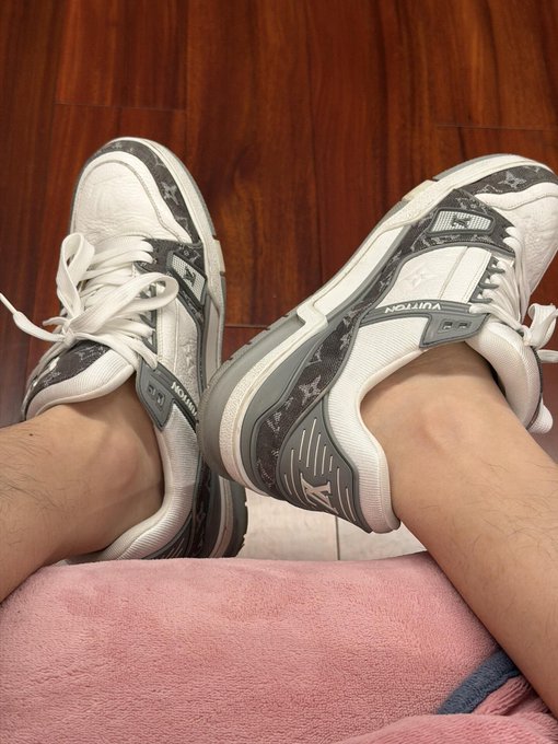 A first-person view shows a person wearing white and gray Vulton sneakers with their feet propped up on a pink blanket.