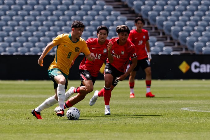 A soccer match showing a player in a yellow and green #9 jersey dribbling the ball while being pursued by three players in red jerseys (#16, #20, #18) on a green field.