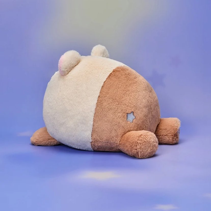 A fluffy plush toy with cream and tan coloring, featuring small ears, a star emblem, and stubby limbs, viewed from behind against a dreamy pastel purple background. The round, cuddly design aligns with the post's description of a "bamjji" being reminiscent of Jisung's soft, charming aesthetic.