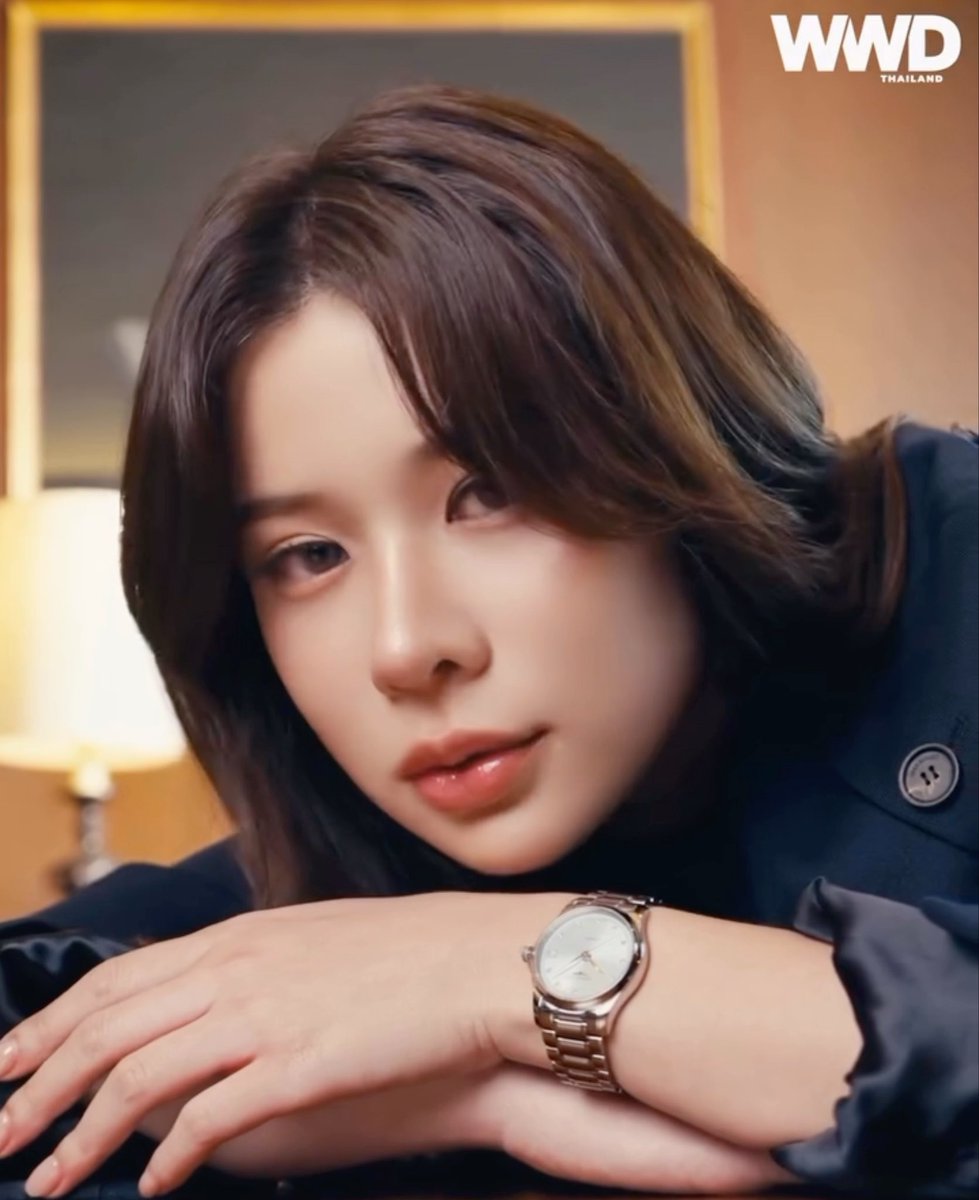 A close-up portrait of a woman with short brown hair, wearing a navy top and a silver wristwatch, with a 'WWD THAILAND' logo in the corner.