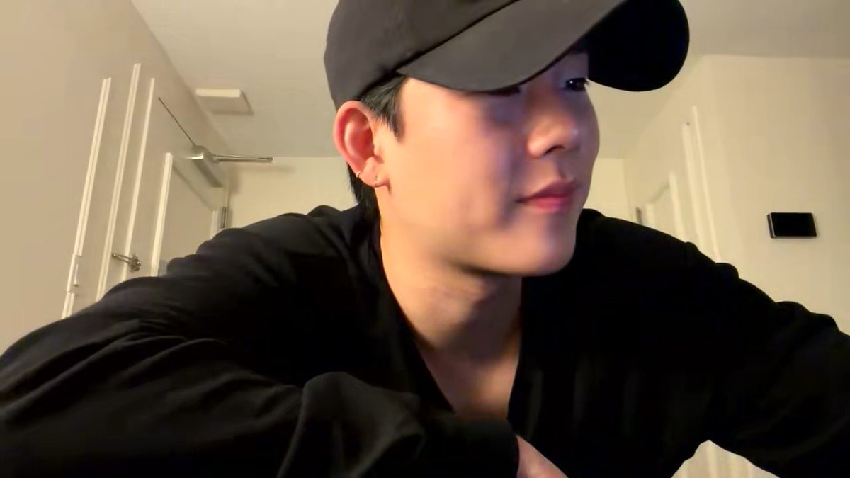 A selfie-style photo of a young man wearing a black cap and black shirt in a brightly lit room with white doors.