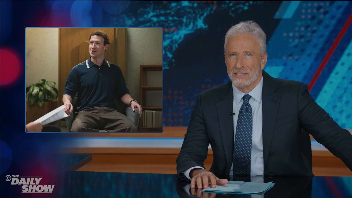 A scene from 'The Daily Show' featuring host Jon Stewart in a suit at his news desk, with an inset image of Mark Zuckerberg sitting in a chair during what appears to be an interview.