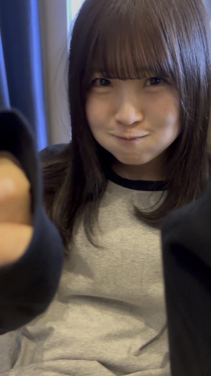 A selfie of a young woman with long brown hair and bangs, wearing a gray and black raglan shirt.