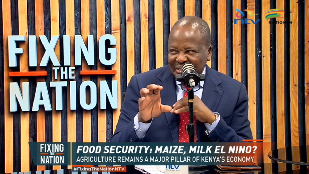 A man in a blue suit and red tie speaks into a microphone on NTV's "Fixing the Nation" program, with on-screen text reading "FOOD SECURITY: MAIZE, MILK EL NINO? AGRICULTURE REMAINS A MAJOR PILLAR OF KENYA'S ECONOMY" and the hashtag #FixingTheNationNTV. The image relates to the post about Agriculture CS Mutahi Kagwe discussing the milk shortage, attributing it to drought and panic buying rather than Foot-and-Mouth Disease.