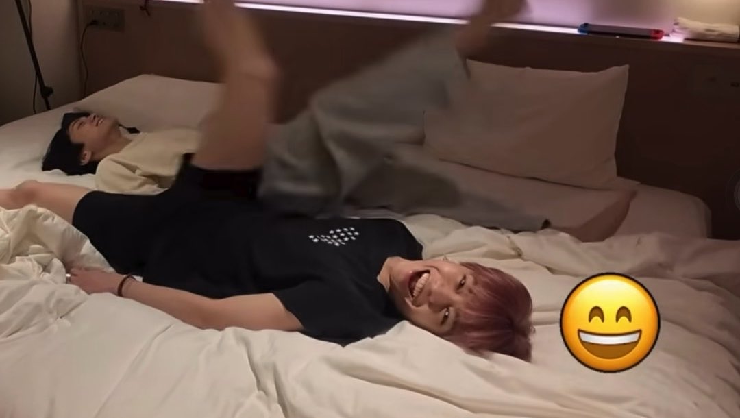 The image shows two young men playfully wrestling on a hotel bed, with one laughing as the other flips over him, accompanied by a smiling emoji. The hashtag "#元気なくなった時用宮武颯" translates to "For when you're feeling down, Miyatake Hayate," suggesting the post serves as a cheerful mood-booster featuring Hayate Miyatake's playful moment.