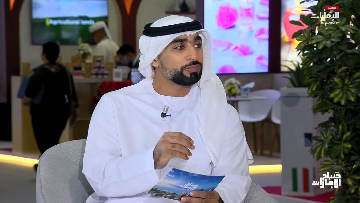 A man in traditional Emirati attire (white kandura and ghutra) holding a brochure during an interview on the Al Emarat TV program 'Manarat'.