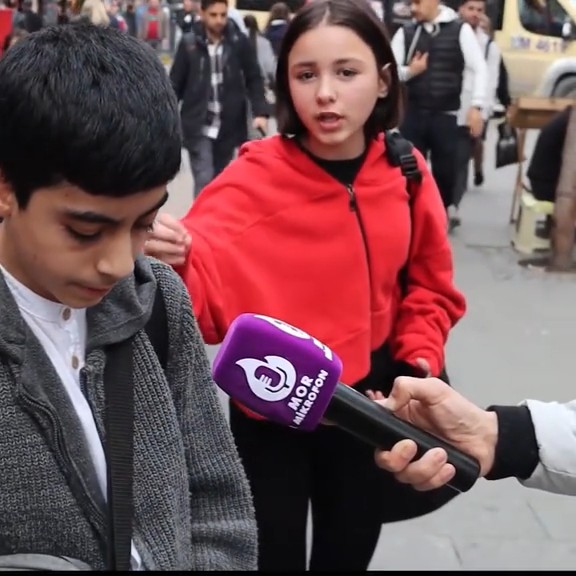 Two children standing on a street being interviewed by someone holding a purple microphone with the text 'NƏR MİN BİR GÜN' / 'MOR MILE GÜN'.