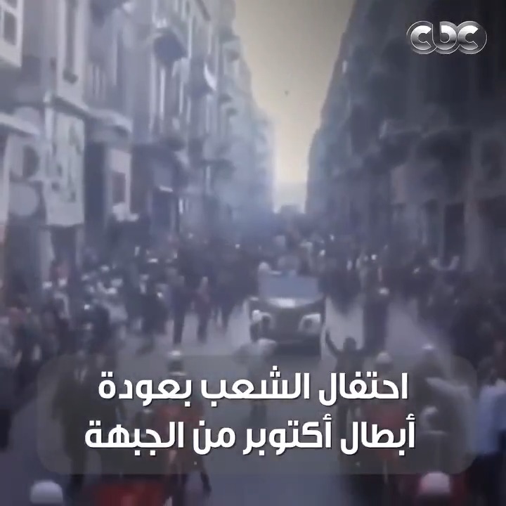 A low-quality video still from a CBC broadcast shows a crowd gathered on a smoke-filled street with Arabic text overlay reading 'احتفال الشعب بعودة أبطال أكتوبر من الجبهة'.