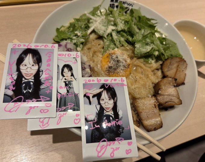 Signed polaroid photos dated '20.6.10.6' rest on a bowl of ramen with greens and chashu pork, alongside chopsticks and a small dish of sauce.