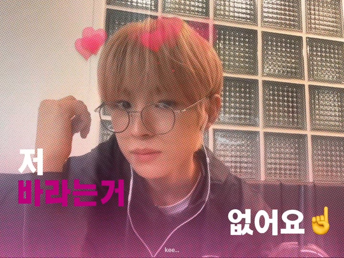 The image shows a young man with reddish hair and round glasses, resting his hand near his face with a serious expression, appearing to be in a video call or stream setting with a glass block wall behind him. Korean text overlays the image reading "저 바라보는거 없어요" (meaning "Don't look at me"), with two red hearts floating above his head, which humorously contradicts his statement while relating to the post's theme of dating conditions.