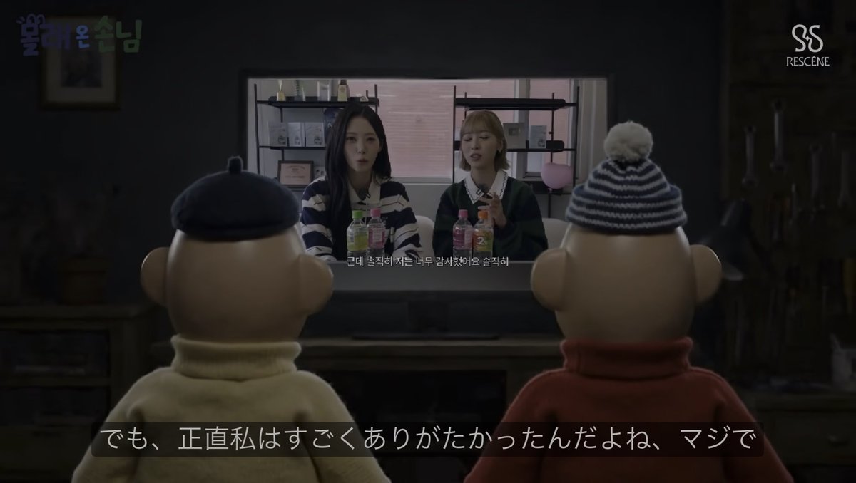 A scene from the Korean show '뿅뿅 어라운드' (PLAY) on RESCENE channel, showing two puppet figures with knit hats watching two women on a TV screen, with Japanese text 'でも、正直私はすごくありがたかったんだよね、マジで' and Korean subtitles visible.