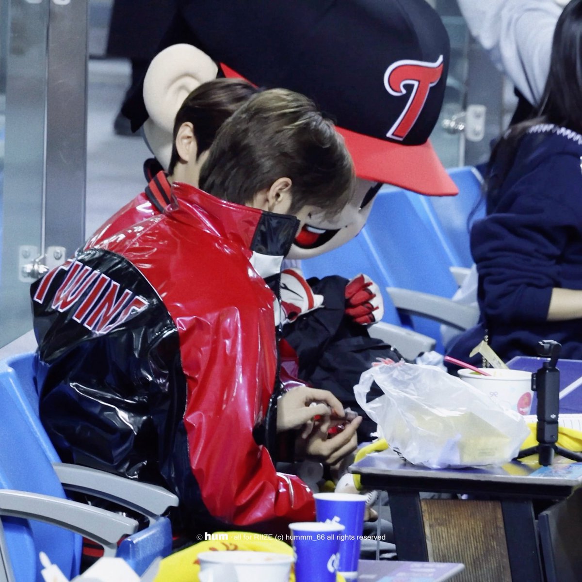 A young fan wears a red and black jersey with 'LUNA' on the back and a large character head mask at what appears to be a sporting event, with a copyright notice reading 'hum all for PIIIZ (c) humm_66 all rights reserved'.