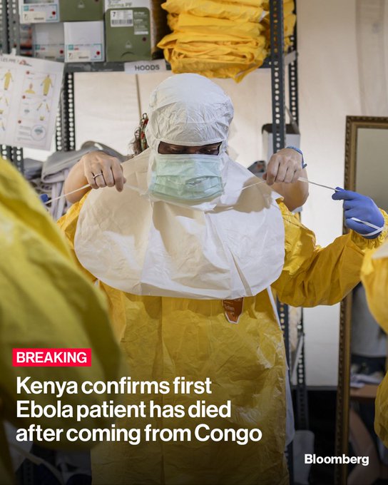 A healthcare worker in protective gear—including a yellow hazmat suit, mask, and hood—adjusts her face covering in what appears to be a medical supply storage area. The Bloomberg graphic overlay reads "BREAKING: Kenya confirms first Ebola patient has died after coming from Congo," directly illustrating the news of the country's first imported Ebola case.