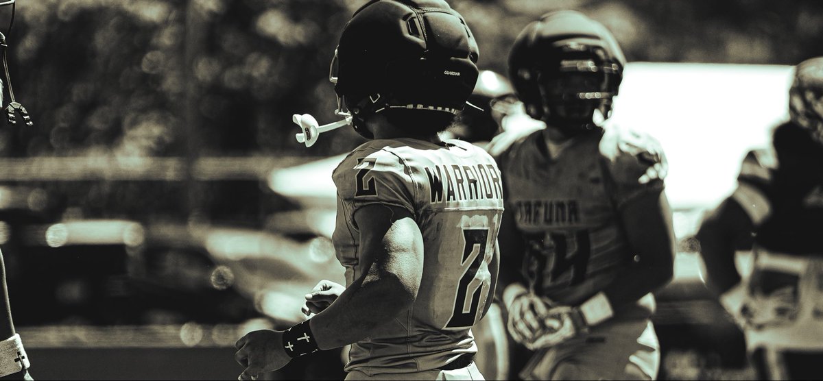 A black-and-white photograph shows a youth football player in a 'Warriors' jersey (number 27) and helmet standing on the field with teammates.