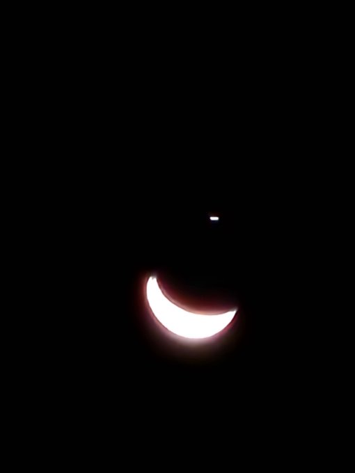 A glowing crescent moon shape glows brightly against a pitch-black background, resembling a crescent roll or moon emoji in the dark.