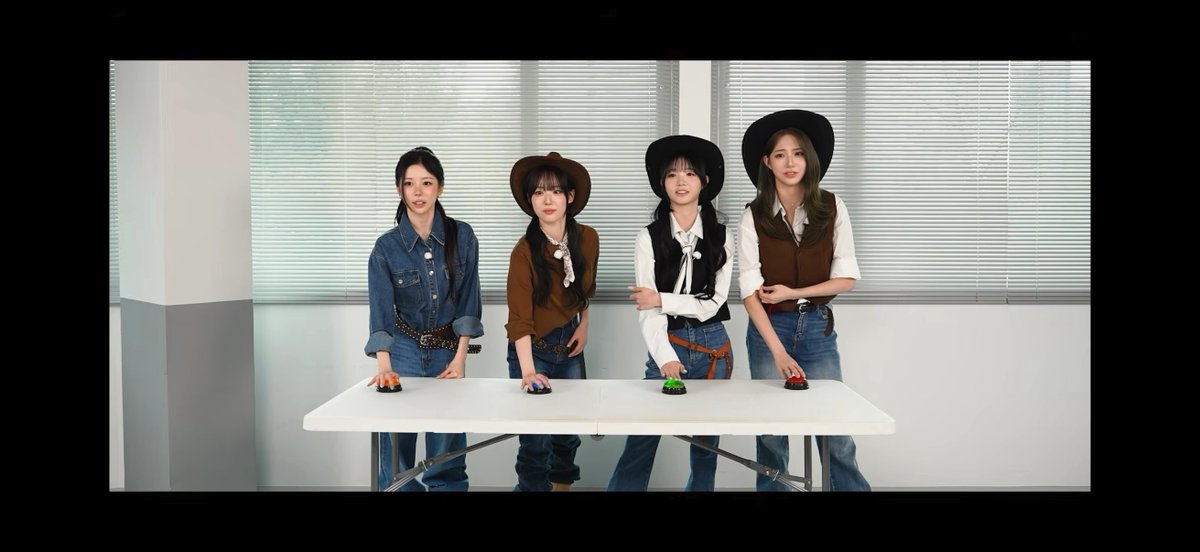 Four young women dressed in western-themed outfits with cowboy hats and denim stand behind a white folding table, each with their hand on a colorful buzzer.