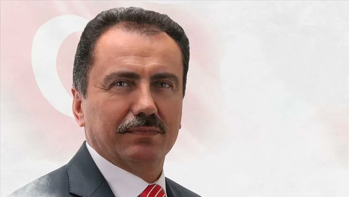 A portrait of a middle-aged man with a mustache wearing a dark suit and red tie against a white background.