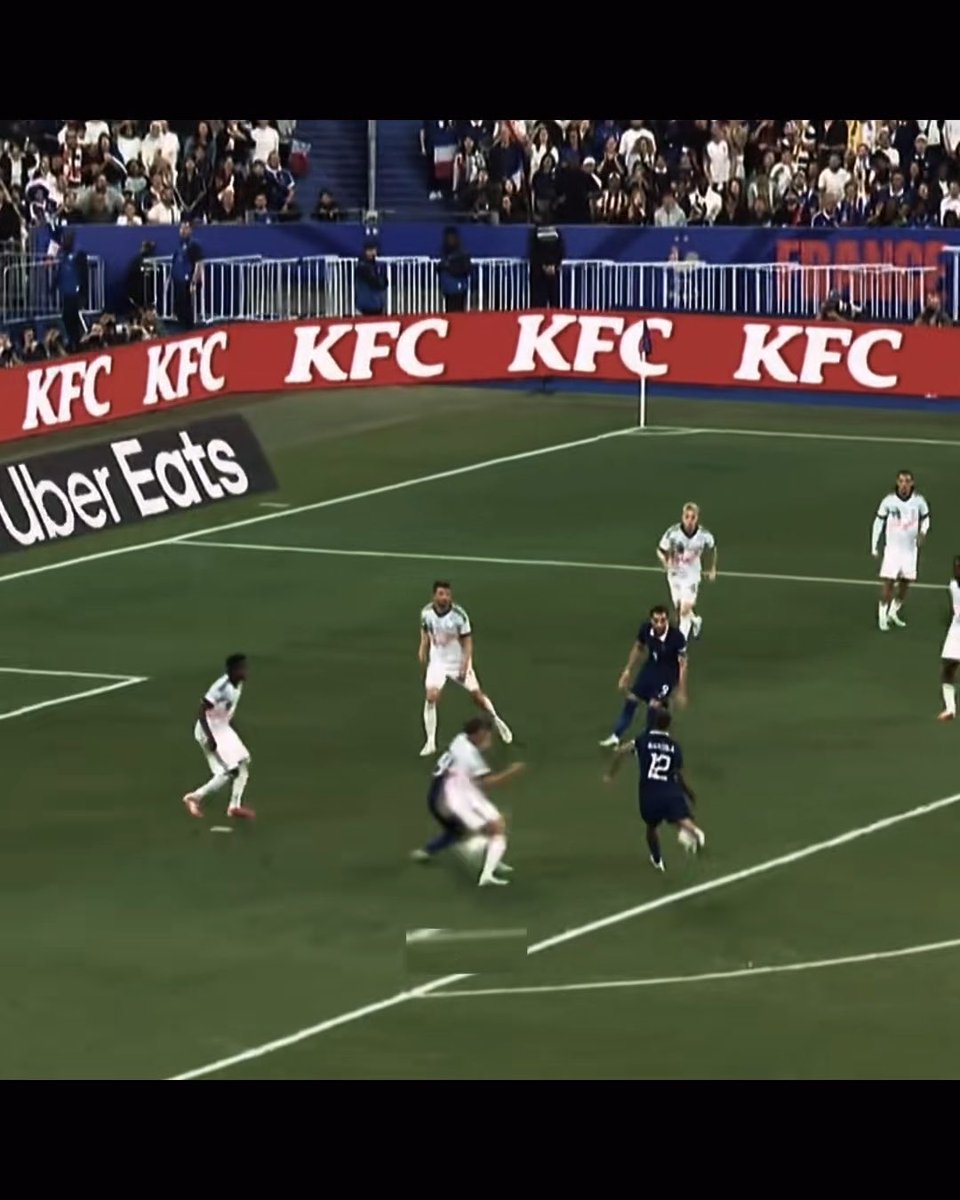 A still from a football match between France and an opposing team in white jerseys, showing players on the pitch with KFC and Uber Eats advertising boards visible along the sidelines.