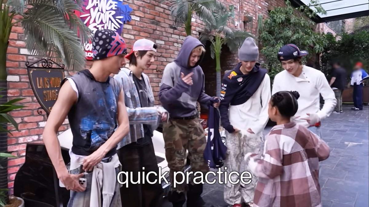 A group of young men in casual streetwear, including hoodies, beanies, and tank tops, are gathered outdoors during what appears to be a 'quick practice' session, as indicated by the caption text.