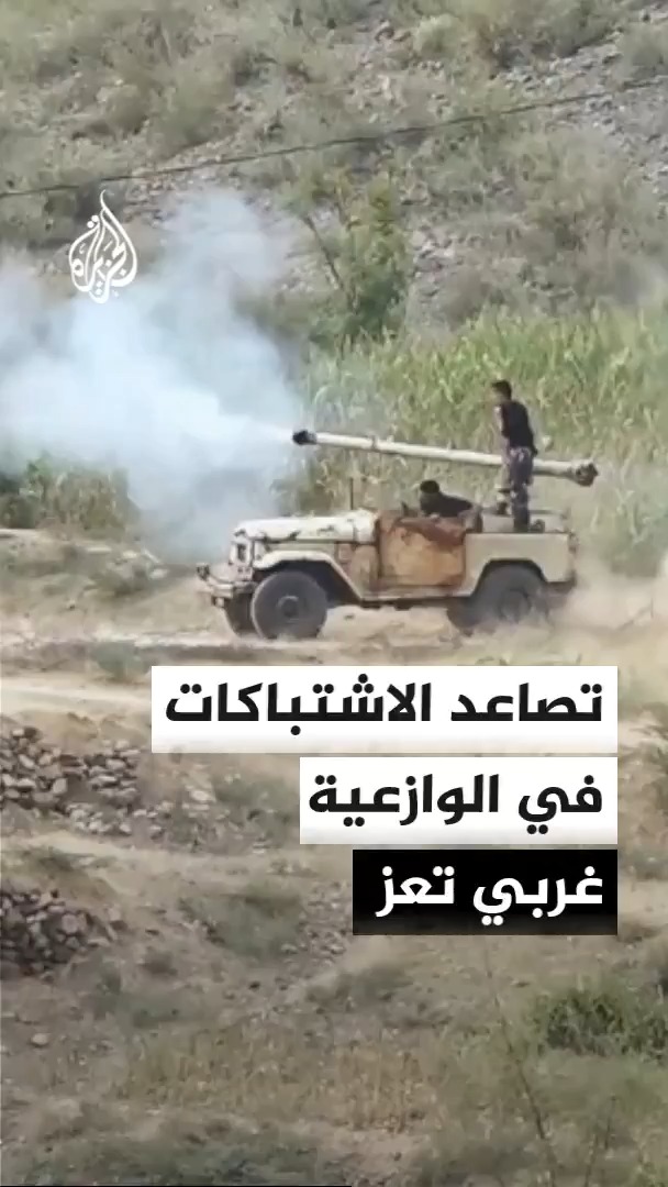 The image shows armed men operating a vehicle-mounted weapon in a mountainous, smoky terrain, consistent with the post describing Yemeni government forces clashing with Houthis near the Al-Waz'iyah district west of Taiz. The Arabic text overlay reads "تصاعد الاشتباكات في الوازعية غربي تعز" (Escalation of clashes in Al-Waz'iyah, west of Taiz), and the Al Jazeera logo is visible in the top left.
