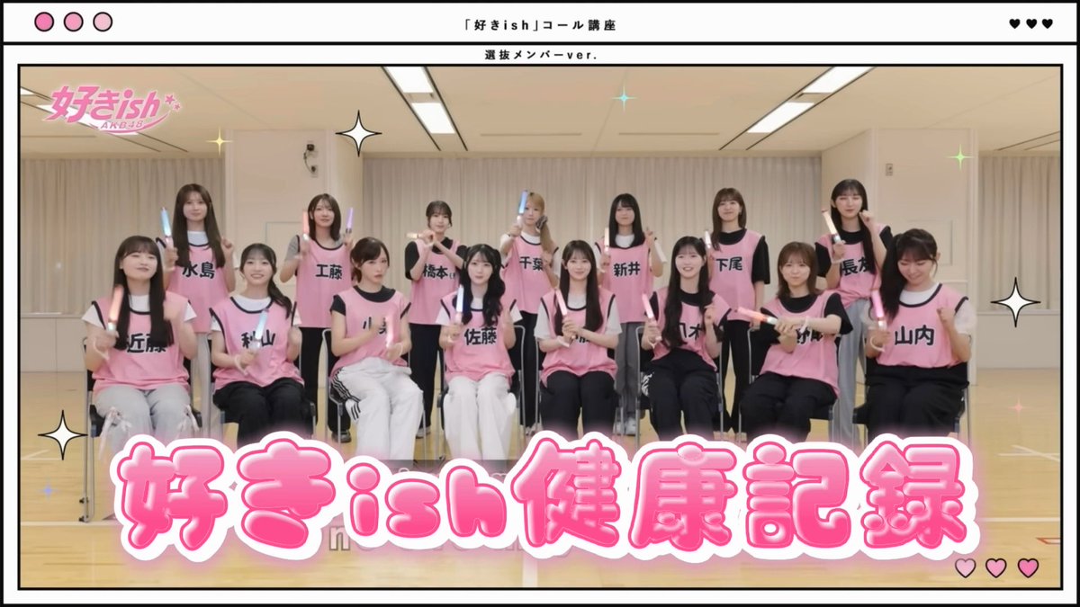 A group of young women wearing pink practice pinnies over black shirts, holding light sticks, with Japanese text reading '「好きish」コール講座' and '好きish健康記録'.