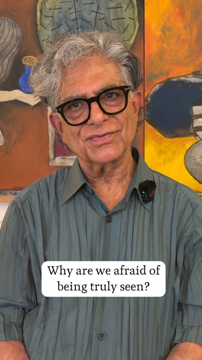 Deepak Chopra speaks directly to the camera in front of a colorful abstract painting, wearing black-rimmed glasses and a striped green shirt with a microphone clipped to his collar. A text overlay reads, "Why are we afraid of being truly seen?"—introducing his reflection on how self-judgment makes vulnerability feel uncomfortable, a theme he explores in The Path to Love Course.