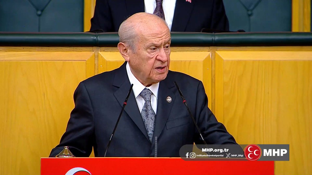 Devlet Bahçeli, leader of Turkey's MHP party, speaking at a podium bearing the MHP logo and 'MHP.org.tr' watermark, with 'MİLLİYETÇİ HAREKET PARTİSİ' social media handles shown.