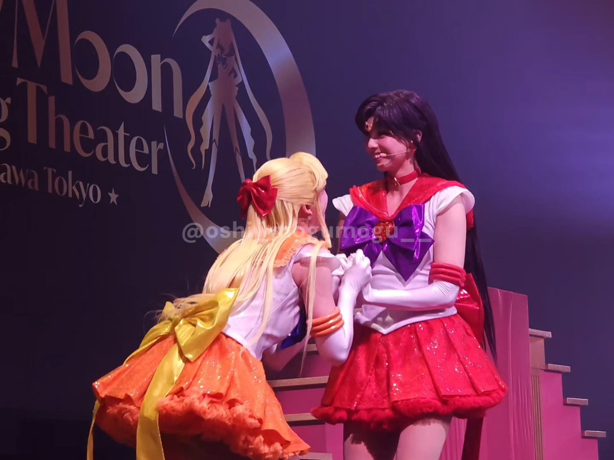 Two cosplayers perform on stage, one dressed as Sailor Moon (orange/yellow) and another as Sailor Mars (red/purple), with a backdrop reading 'Moon Theater' and 'Tokyo'. A watermark '@oshirokokumogu' is visible.
