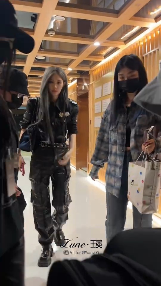 A photo of a woman with silver hair in a black leather outfit walking through what appears to be a Japanese venue, with a watermark reading 'Lune·王珆 All for @WangYi'.