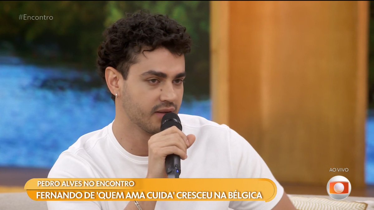 A young man with curly hair speaks into a microphone on the TV show 'Encontro', with the chyron 'Pedro Alves' state 'Fernando de 'Quem Ama Cuida' cresceu na Bélgica' while the Globo 'Ao Vivo' logo is visible.