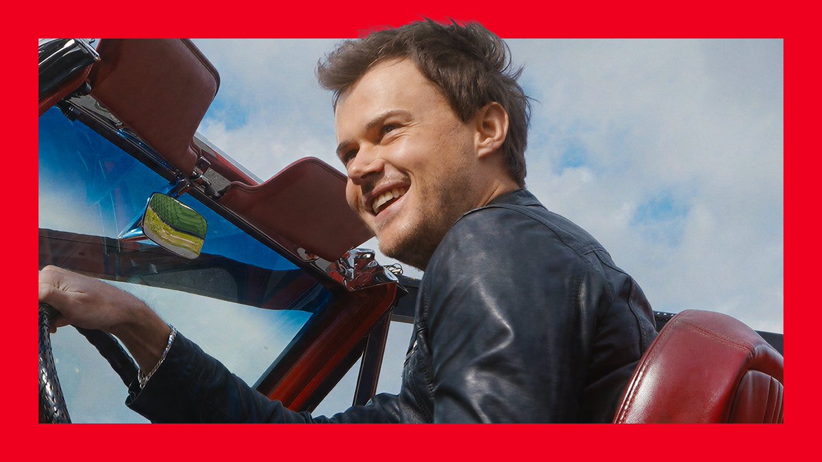 Chris Briney grins joyfully from the driver's seat of a red convertible, his leather jacket catching the light against a bright blue sky. The candid smile perfectly captures the warmth and charm that made viewers "came for the yearning, stayed for the smiles."