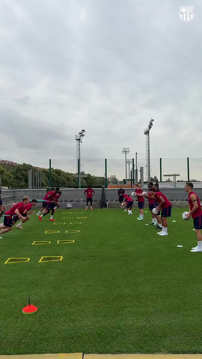 FC Barcelona players in red training kits perform agility drills on a pitch with yellow ladder markers, continuing their preparation work as indicated by the Catalan phrase "La feina no s'atura" (The work doesn't stop), reinforced by the club's crest visible in the top right corner.