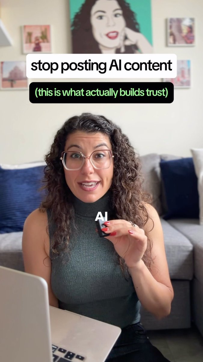 A woman with curly hair and glasses speaking to camera with overlaid text reading 'stop posting AI content' and '(this is what actually builds trust)', holding a small object labeled 'AI'.
