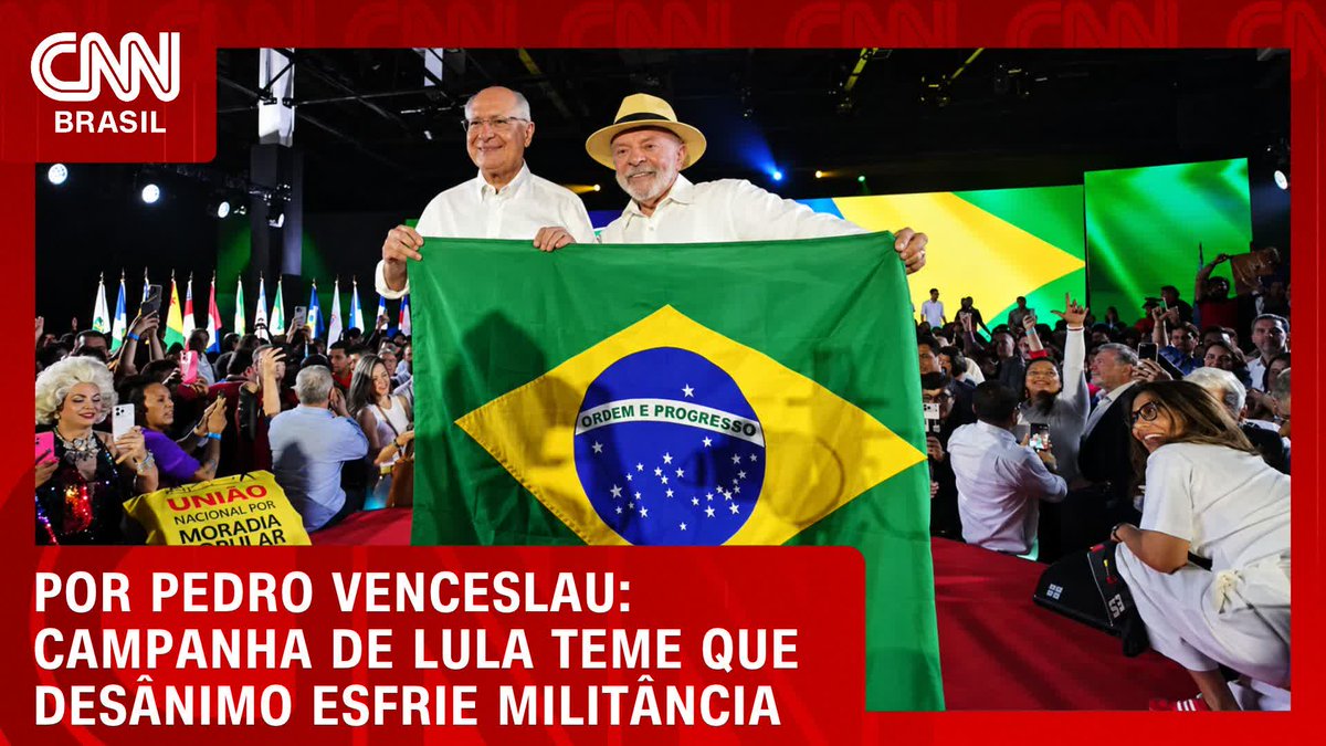 Two men hold up a Brazilian flag at a political rally, with the text on the image reading "Por Pedro Venceslau: Campanha de Lula teme que desânimo esfrie militância" (By Pedro Venceslau: Lula's campaign fears that discouragement will cool militancy), relating to the CNN Brasil segment about concerns over declining enthusiasm among supporters of Lula's political campaign.