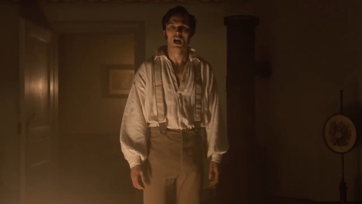 A pale, gaunt figure in a loose period shirt with suspenders stands in a dimly lit room, mouth agape and face contorted in an unnatural expression, embodying a possessed being succumbing to an otherworldly force—much like Lily-Rose Depp's character in NOSFERATU who channels the haunting stillness and tension of butoh dance to convey demonic control.