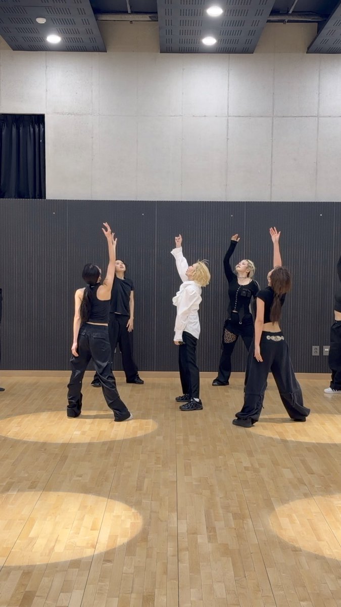 A K-pop dance crew practices a routine in a mirrored studio with one arm lifted toward the ceiling, capturing a rehearsal moment for MINZY's "Calling" dance practice video.