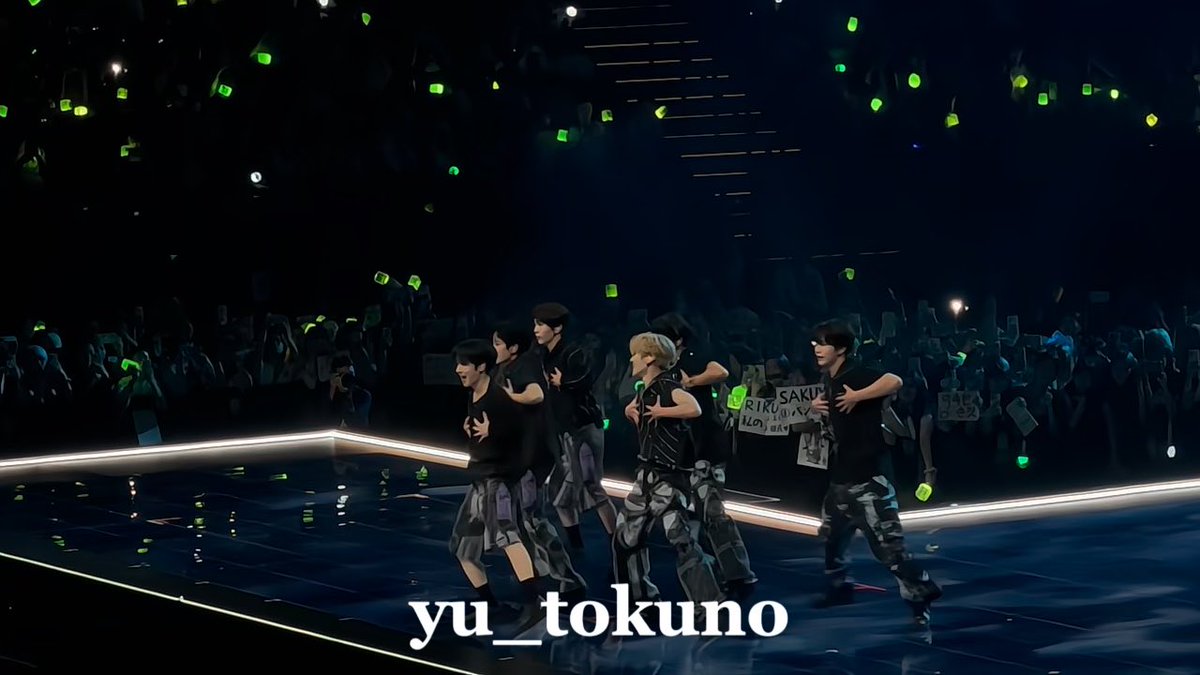 A K-pop group performing on stage with green light sticks glowing in the audience; the watermark reads 'yu_tokuno'.