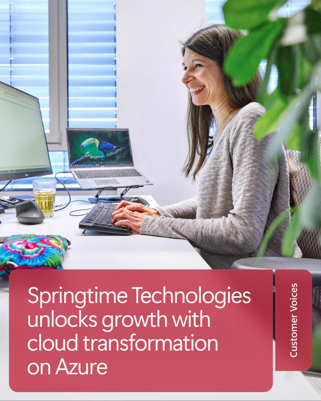 A woman with long brown hair sits at a desk using a computer, smiling while looking at the screen. Two monitors are positioned behind her. A colorful textile is on the desk. Text reads, 'Springtime Technologies unlocks growth with cloud transformation on Azure.'