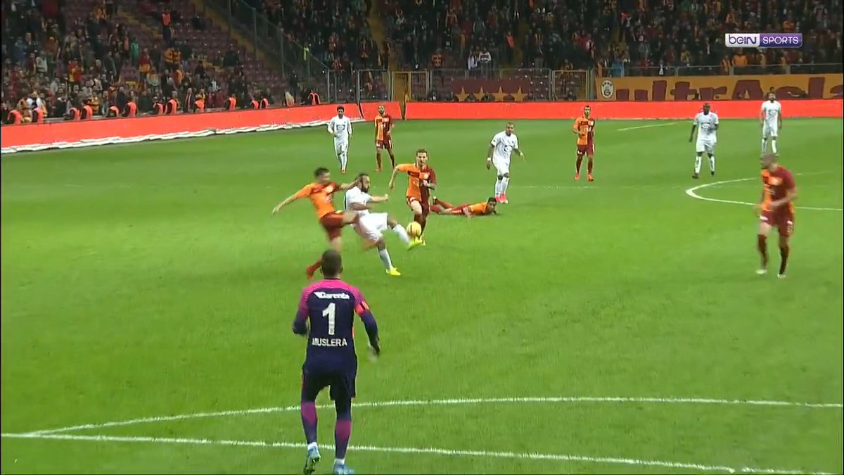 A soccer match in progress shows a player in white unleashing an overhead kick amidst a scramble with defenders in orange and maroon kits, while goalkeeper MUSLERA (#1) stands ready in a pink and purple jersey, all on a green pitch framed by an "Ultra" banner and beIN SPORTS logo. The image captures the exact moment referenced in the caption—Olcan Adın's classic overhead goal in the Süper Lig.